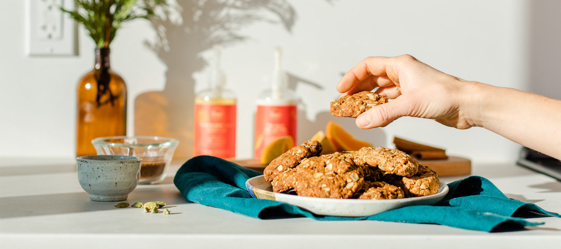 a hand is taking a cookie from a pile on the counter. This holiday cookie recipe is vegan, can be easily made gluten free, is perfect for holiday potluck desserts and is inspired by our Orange Cardamom holiday scent. 