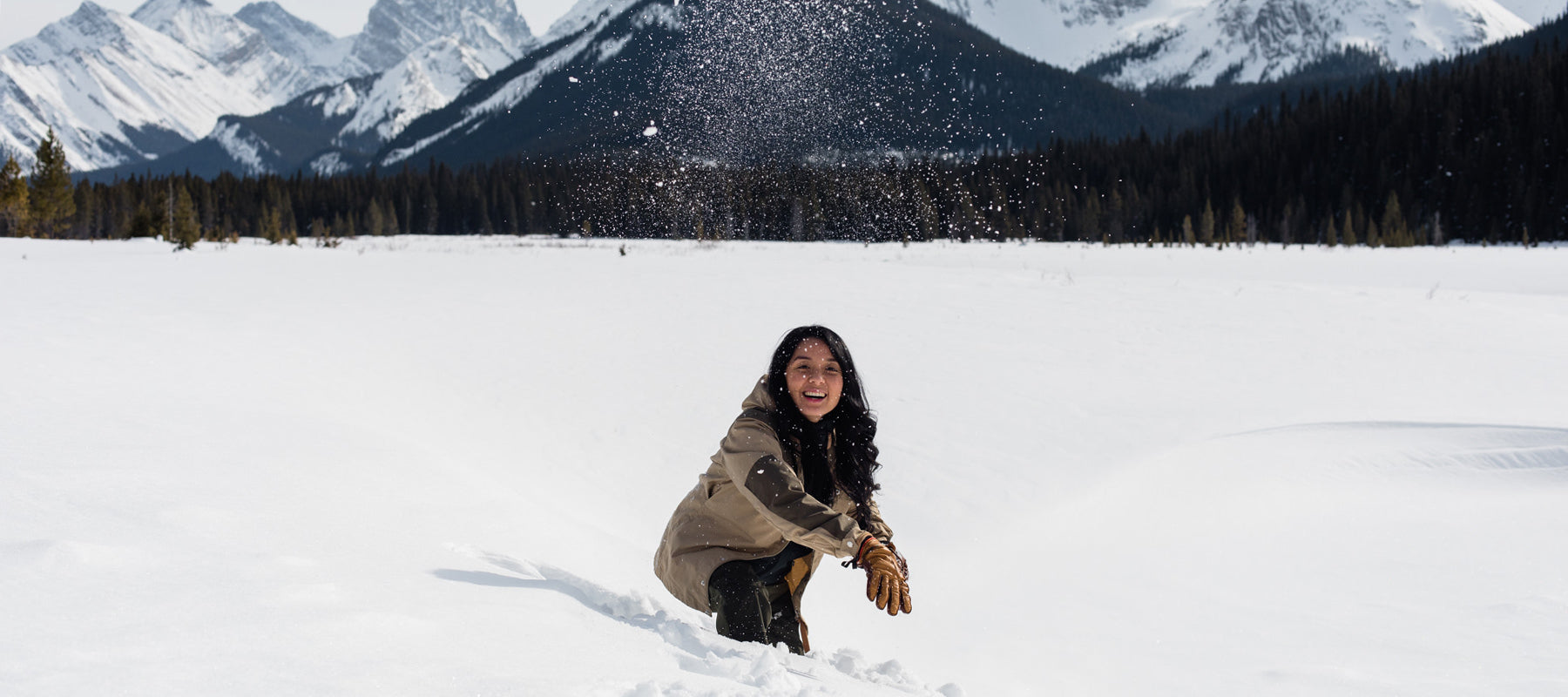 Woman throwing snowball with mountains in the background. 