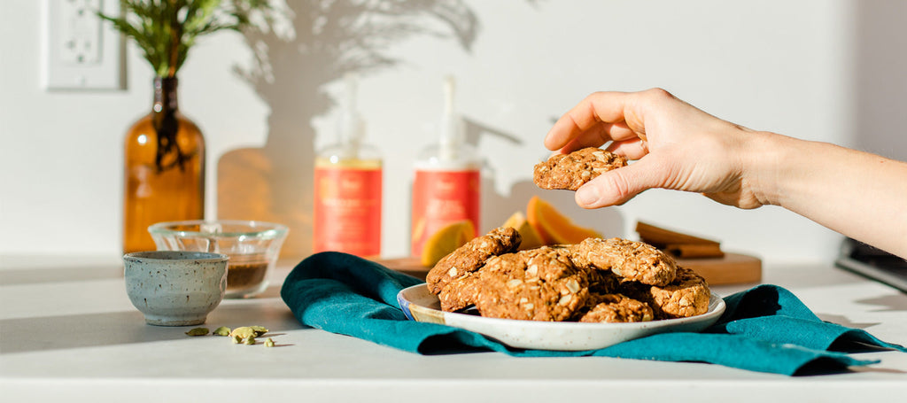 a hand is taking a cookie from a pile on the counter. This holiday cookie recipe is vegan, can be easily made gluten free, is perfect for holiday potluck desserts and is inspired by our Orange Cardamom holiday scent.