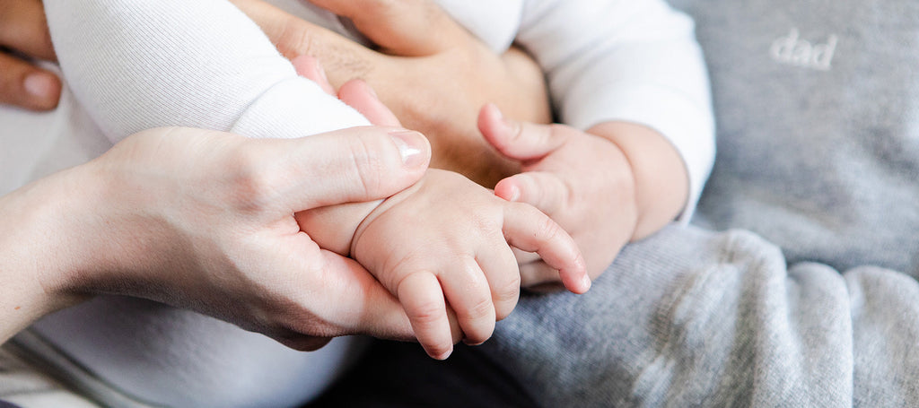 An adult hand holding a baby hand.