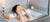 Woman in bath with orange slices on her eyes. On the side of the tub are Canadian local Rocky Mountain Soap Company natural bar soap, bath bomb and body scrub.  