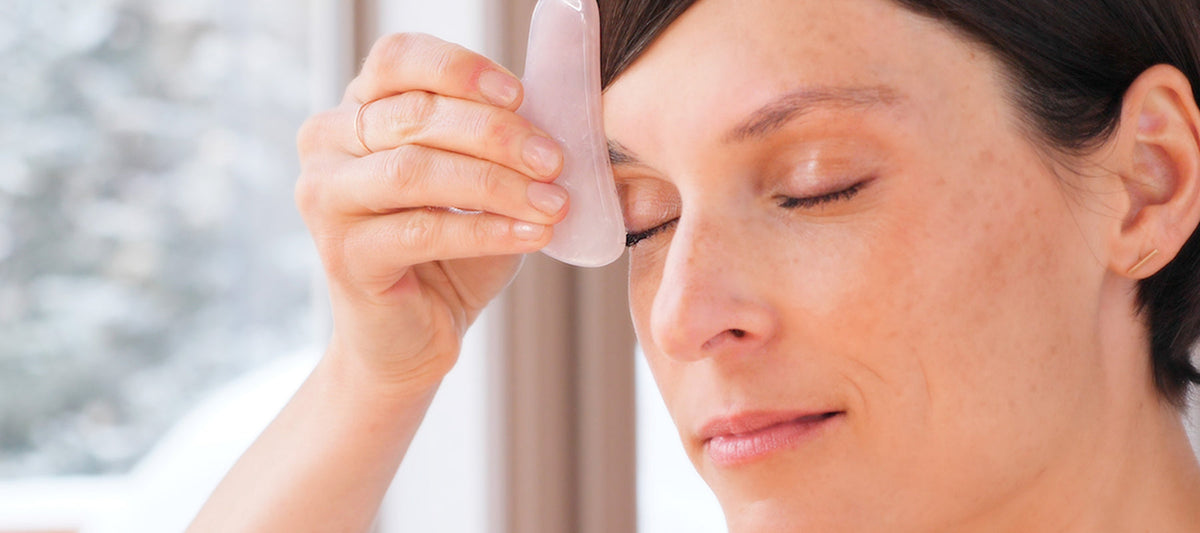 image of woman using Gua Sha tool on her skin.