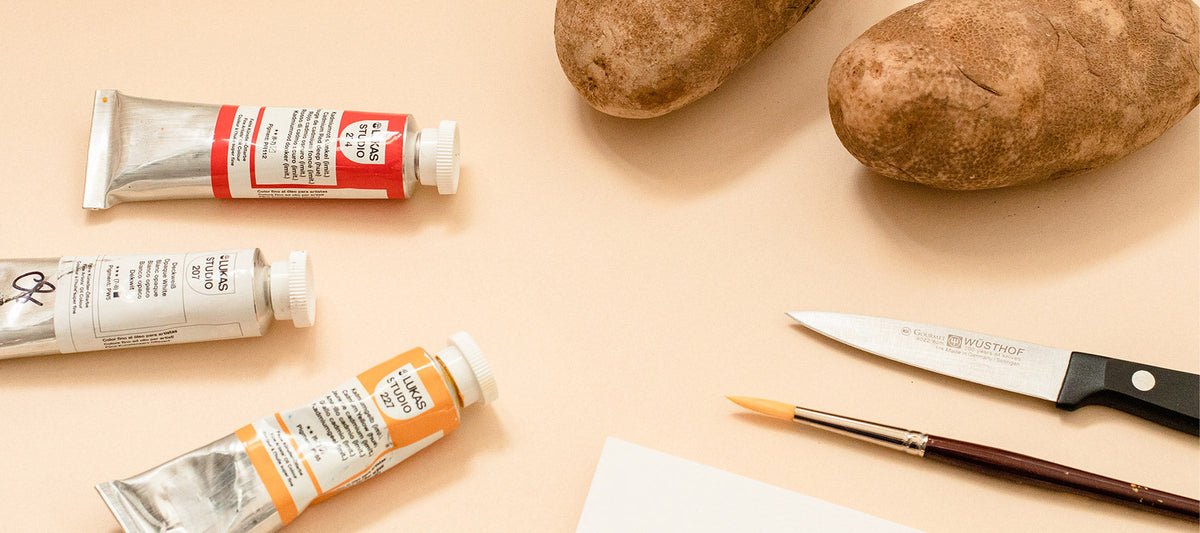 Image of paint, paint brush, potatos, knife and paper to make a DIY holiday card potato stamp.