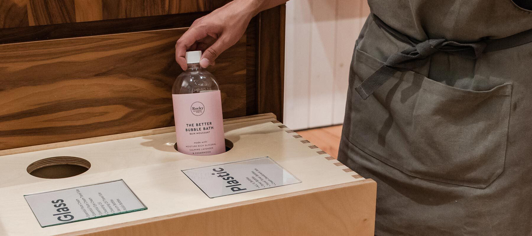 Image of an empty plastic 1L Rocky Mountain Soap Company bottle being placed into a bin. 