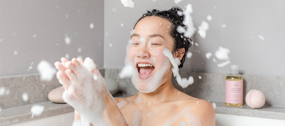 Woman clapping bubbles together laughing in bath.