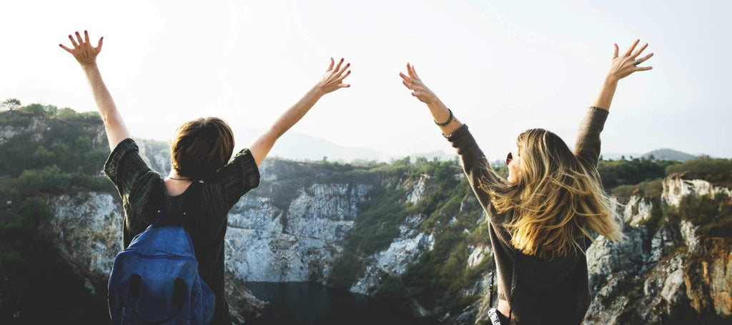 girlfriends with their arms up overlooking a beautiful landscape.