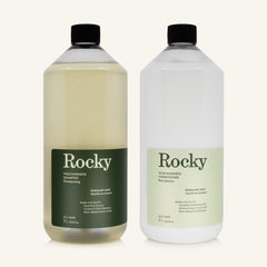 Two 1L bottles of Rocky Wild Kindness Shampoo and Conditioner in rosemary mint for normal hair, centered on a light cream background.