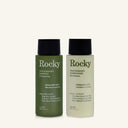 Two 90ml bottles of Rocky Wild Kindness Shampoo and Conditioner in rosemary mint for normal hair, featuring a olive green bottles with black caps, centered on a light cream background.