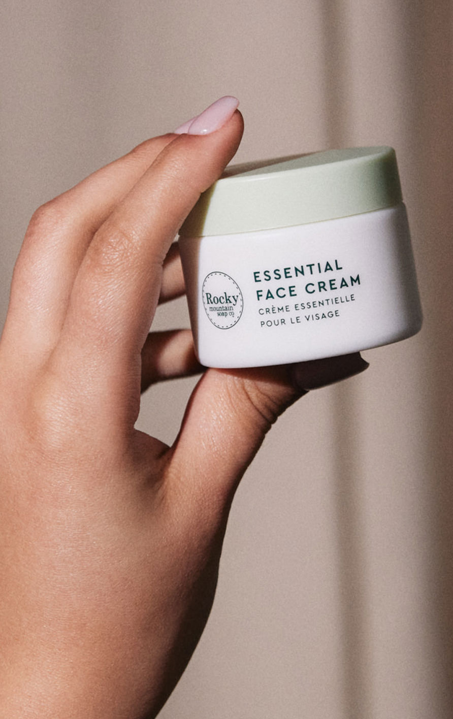 a hand holding a container of essential face cream