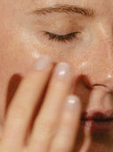 Close-up of a hand gently applying Essential Face Cream & Hydrating Natural Face Serum to a cheek.