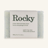 Handcrafted cold-process Rocky Mountain Soap Company Minty Tea Tree bar soap, translucent with blue speckles, in a label with weight details in English and French.