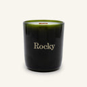 A dark green Moonlight Candle by Rocky Mountain Soap Company in a glass jar with a wooden wick, featuring the word Rocky printed in gold on the front.