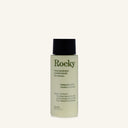 A bottle of Rocky Wild Kindness Conditioner in Rosemary Mint scent, featuring a pale yellow-green translucent bottle, dark green text, and a black cap, set against a solid off-white background.