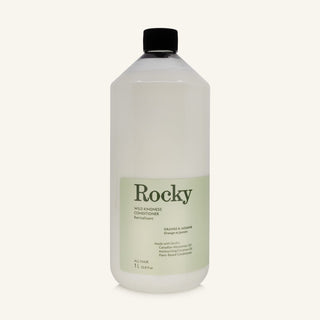 A 1L bottle of Rocky Wild Kindness Conditioner in Orange & Jasmine scent with a black cap and a light green label, centered on a warm off-white background.