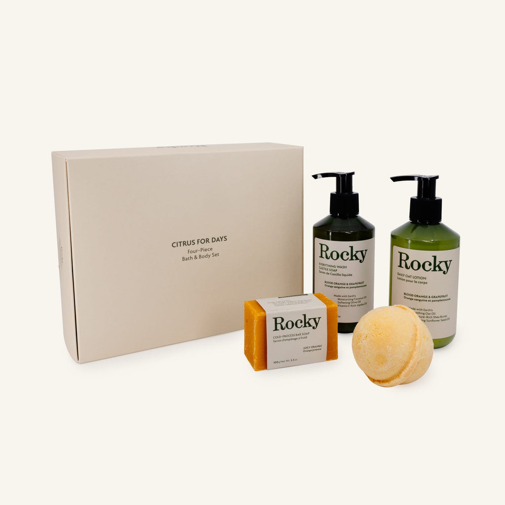 Rocky Citrus for Days bath and body gift set featuring a cream-colored gift box, a bar of juicy orange soap, a juicy orange bath bomb, and two pump bottles (blood orange and grapefruit everything wash and oat lotion).