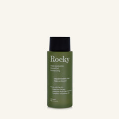 A 90ml bottle of Rocky Wild Kindness Shampoo in Cedarwood & Lime for dry hair, featuring an olive green bottle and a black cap, centered on a light cream background.