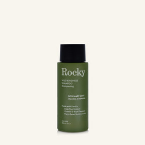A 90ml bottle of Rocky Wild Kindness Shampoo in Rosemary Mint for normal hair, featuring an olive green bottle and a black cap, centered on a light cream background.