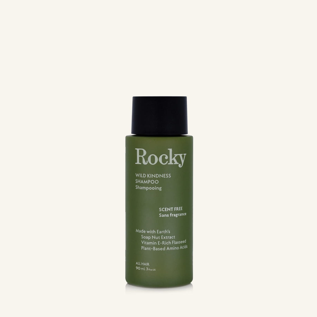 A 90ml bottle of Rocky Wild Kindness Shampoo in scent free for normal hair, featuring an olive green bottle and a black cap, centered on a light cream background.