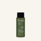 A 90ml bottle of Rocky Wild Kindness Shampoo in scent free for normal hair, featuring an olive green bottle and a black cap, centered on a light cream background.