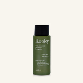 A 90ml bottle of Rocky Wild Kindness Shampoo in scent free for normal hair, featuring an olive green bottle and a black cap, centered on a light cream background.