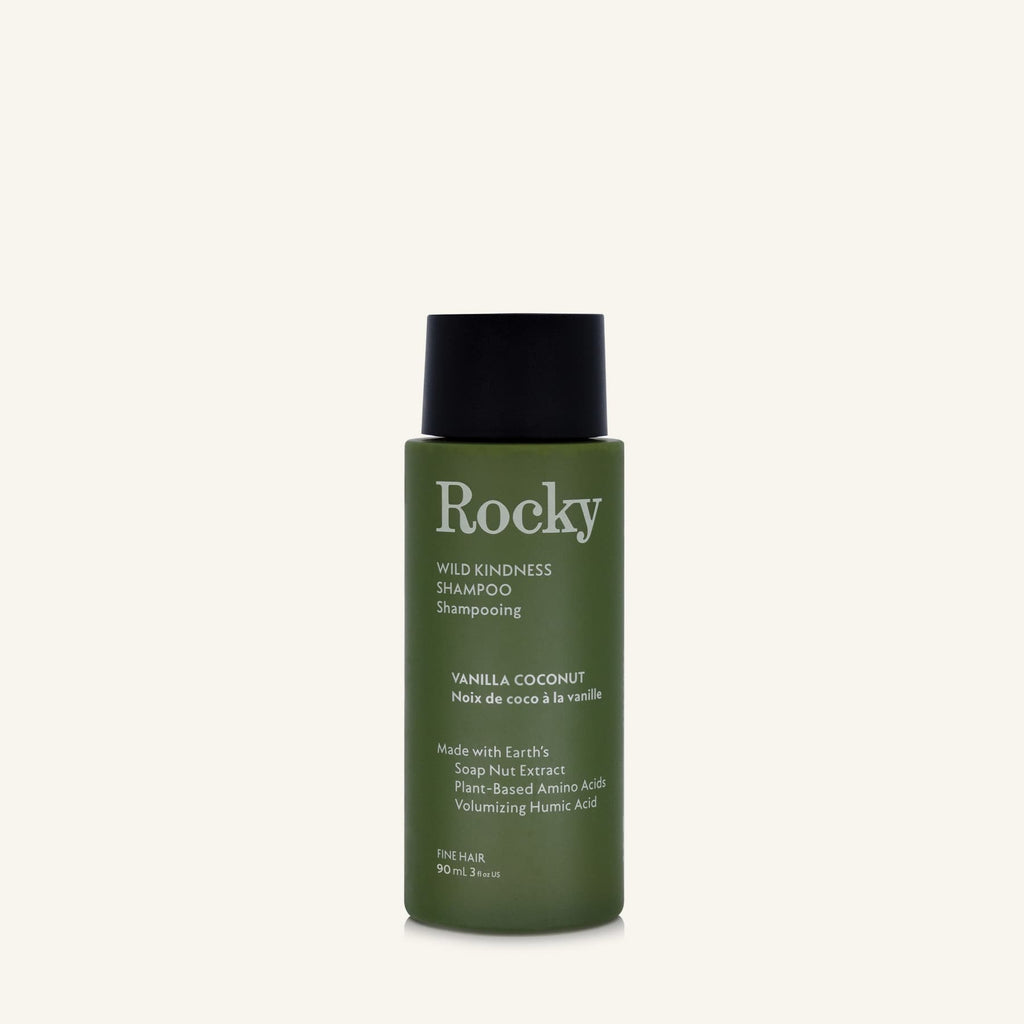 A 90ml bottle of Rocky Wild Kindness Shampoo in Vanilla Coconut for fine hair, featuring an olive green bottle and a black cap, centered on a light cream background.