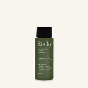 A 90ml bottle of Rocky Wild Kindness Shampoo in Vanilla Coconut for fine hair, featuring an olive green bottle and a black cap, centered on a light cream background.