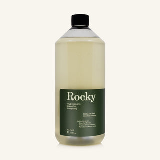 A 1L bottle of Rocky Wild Kindness Shampoo in Rosemary Mint for normal hair, featuring an olive green bottle and a black cap, centered on a light cream background.