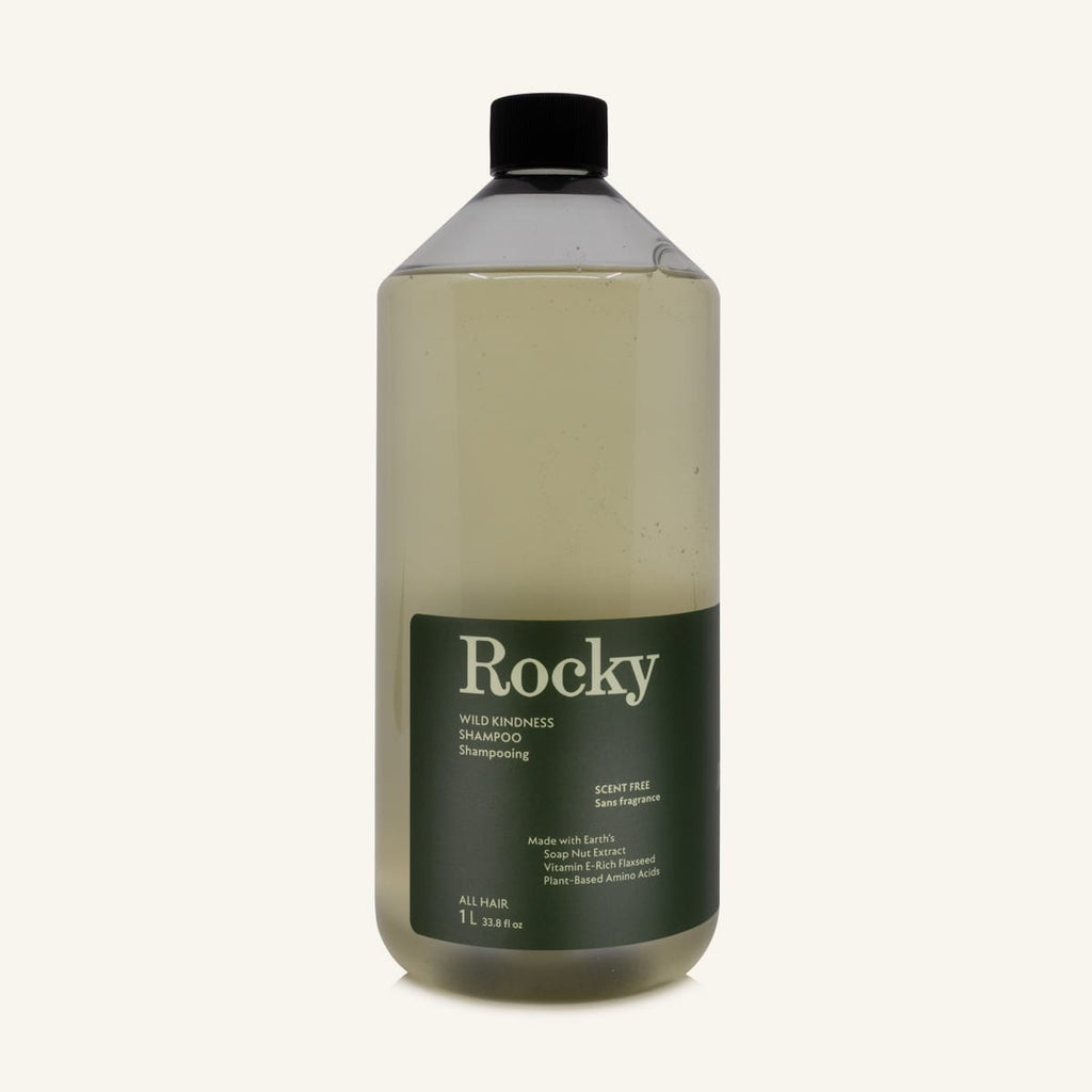 A 1L bottle of Rocky Wild Kindness Shampoo in scent free for normal hair, featuring an olive green bottle and a black cap, centered on a light cream background.