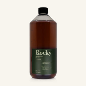 A 1L bottle of Rocky Wild Kindness Shampoo in Vanilla Coconut for fine hair, featuring an olive green bottle and a black cap, centered on a light cream background.