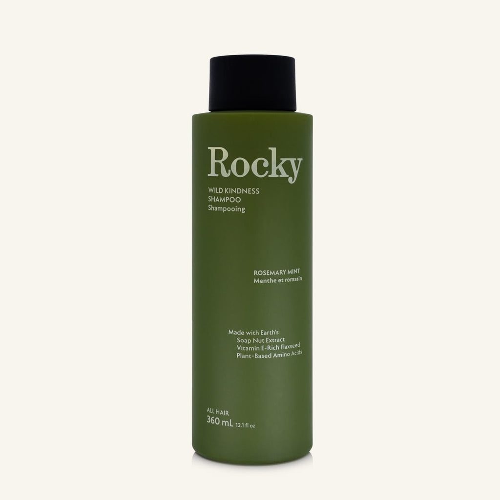 A 360ml bottle of Rocky Wild Kindness Shampoo in Rosemary Mint for normal hair, featuring an olive green bottle and a black cap, centered on a light cream background.