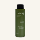 A 360ml bottle of Rocky Wild Kindness Shampoo in Rosemary Mint for normal hair, featuring an olive green bottle and a black cap, centered on a light cream background.