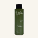 A 360ml bottle of Rocky Wild Kindness Shampoo in scent free for normal hair, featuring an olive green bottle and a black cap, centered on a light cream background.
