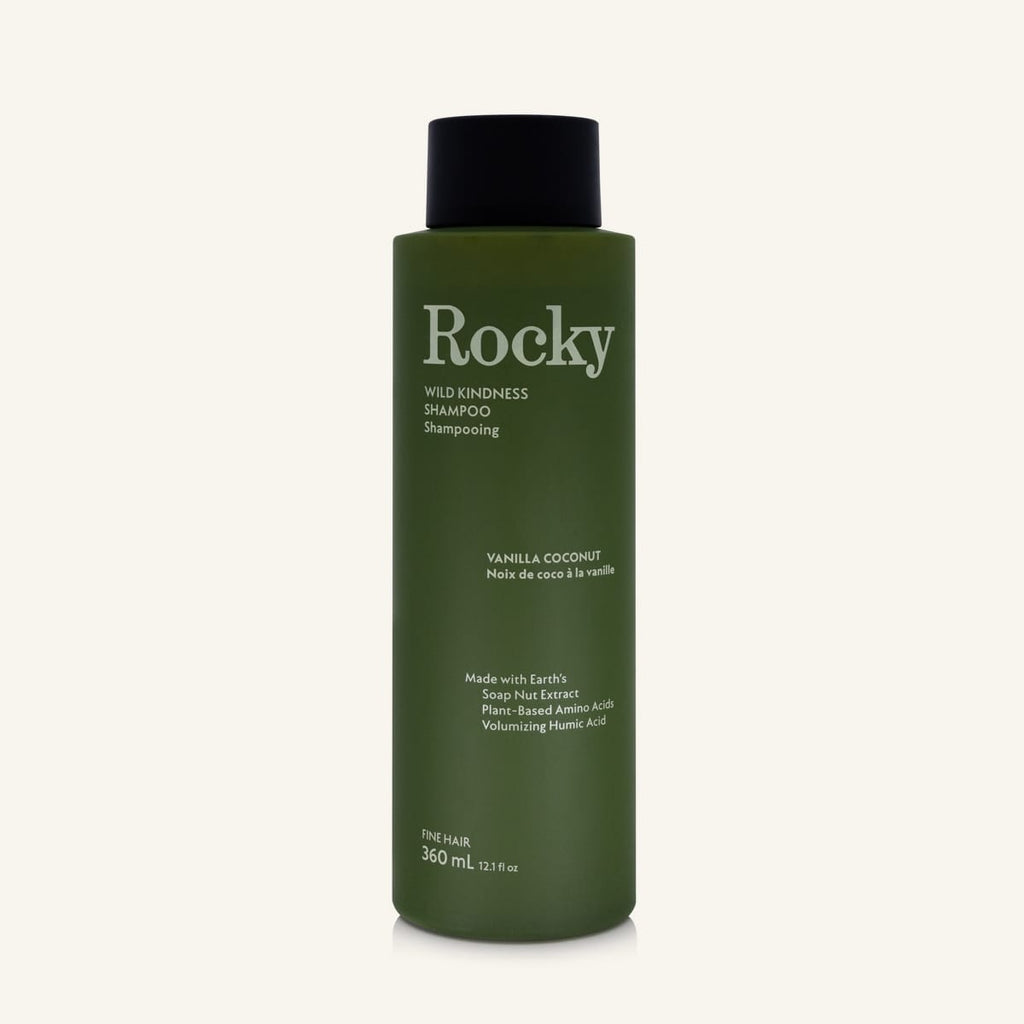 A 360ml bottle of Rocky Wild Kindness Shampoo in Vanilla Coconut for fine hair, featuring an olive green bottle and a black cap, centered on a light cream background.