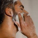 A person using a lathered Rocky Mountain Soap Company Hair Bar: Solid Shampoo enriched with strengthening rice protein to wash their bearded jawline.