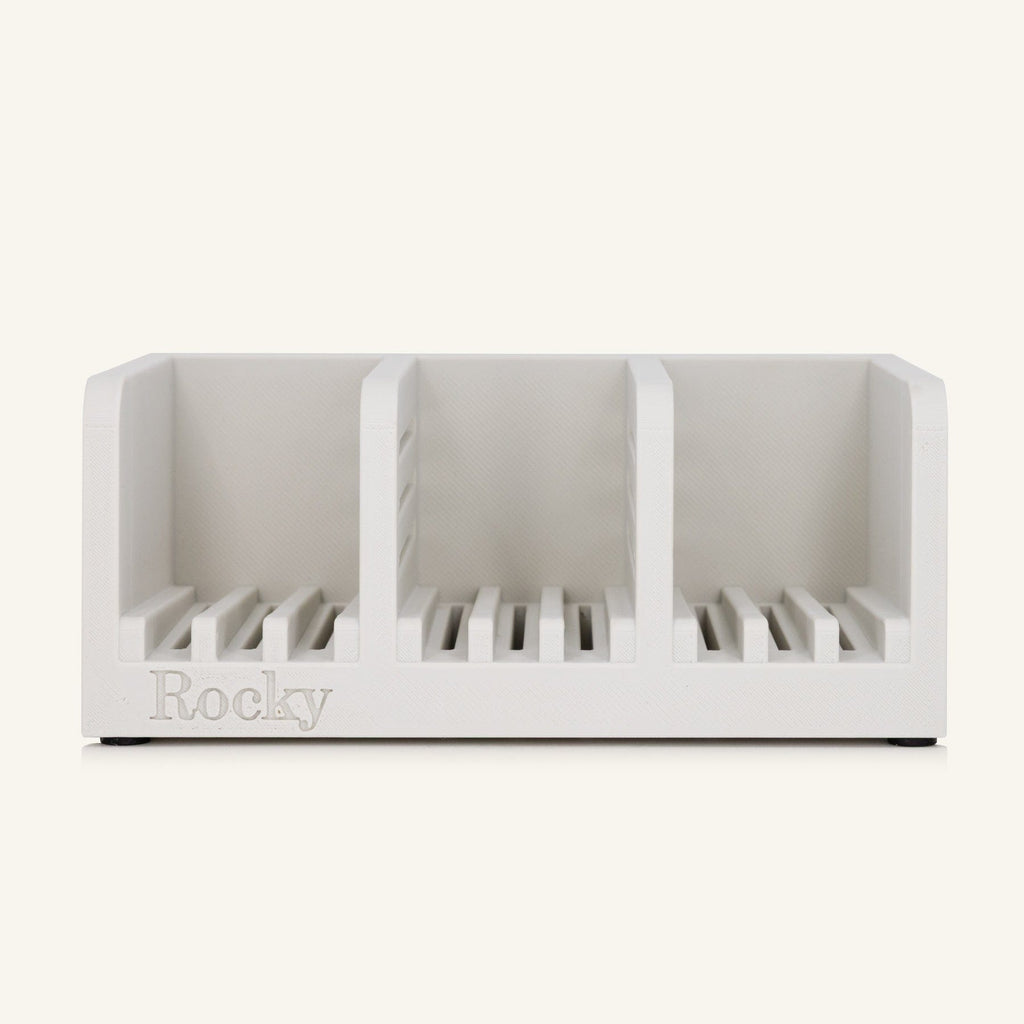 A white three-compartment soap holder with slotted bases and the name 'Rocky' embossed on the front, shown against a solid off-white background.