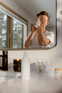 A person reflected in a bathroom mirror uses a velvety smooth organic Bamboo Face Cloth to wipe their face.