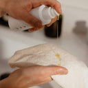 A person dispensing liquid from a white pump bottle onto a velvety smooth Relaxus Bamboo Face Cloth held in their hands.