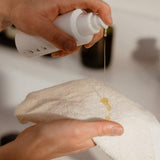 A person dispensing liquid from a white pump bottle onto a velvety smooth Relaxus Bamboo Face Cloth held in their hands.