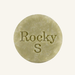 A round, green solid shampoo hair bar embossed with the text 'Rocky S, centered on a solid cream background.