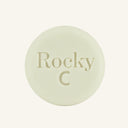 A round, white solid conditioner hair bar embossed with the text 'Rocky C, centered on a solid cream background.