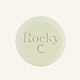 A round, white solid conditioner hair bar embossed with the text 'Rocky C, centered on a solid cream background.