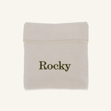 A small off-white fabric pouch with the name 'Rocky' printed in dark olive green text, shown on a plain light beige background.