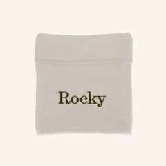A small off-white fabric pouch with the name 'Rocky' printed in dark olive green text, shown on a plain light beige background.