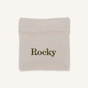 A small off-white fabric pouch with the name 'Rocky' printed in dark olive green text, shown on a plain light beige background.