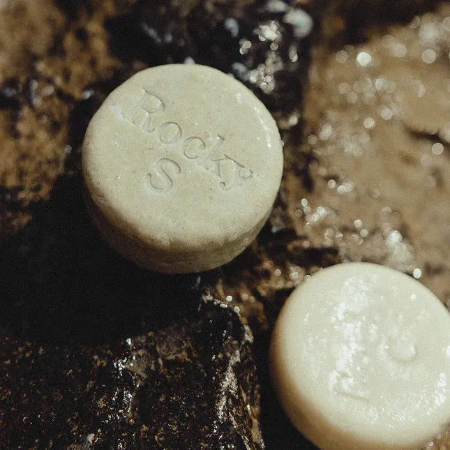 Two unwrapped Rocky shampoo bars resting on wet rock