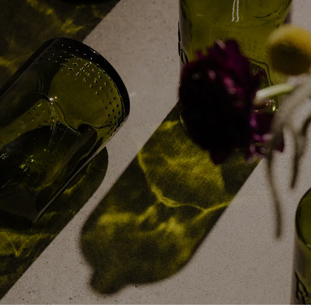 Empty green glass bottles casting long shadows on a pale surface