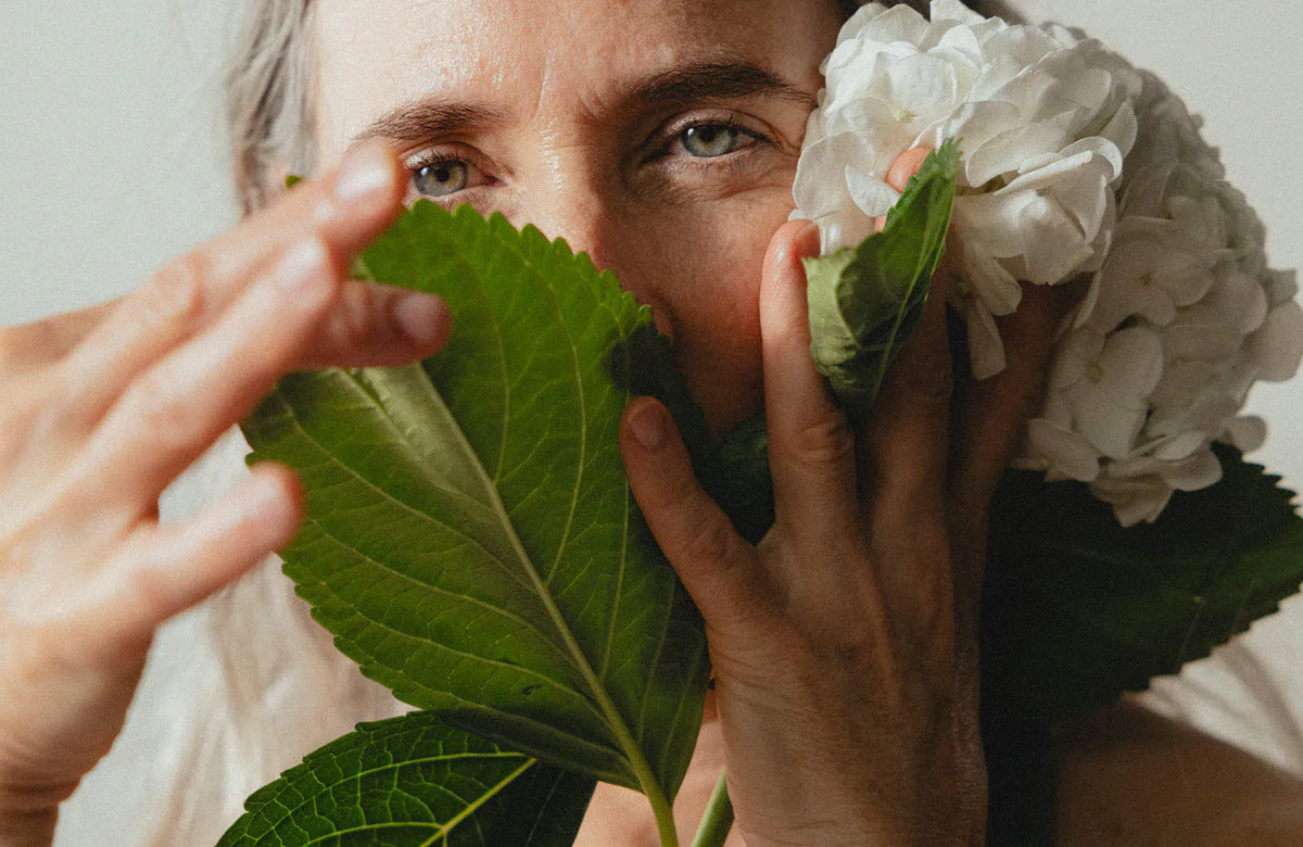 A woman holding hydrangea leaves and blossom to her face