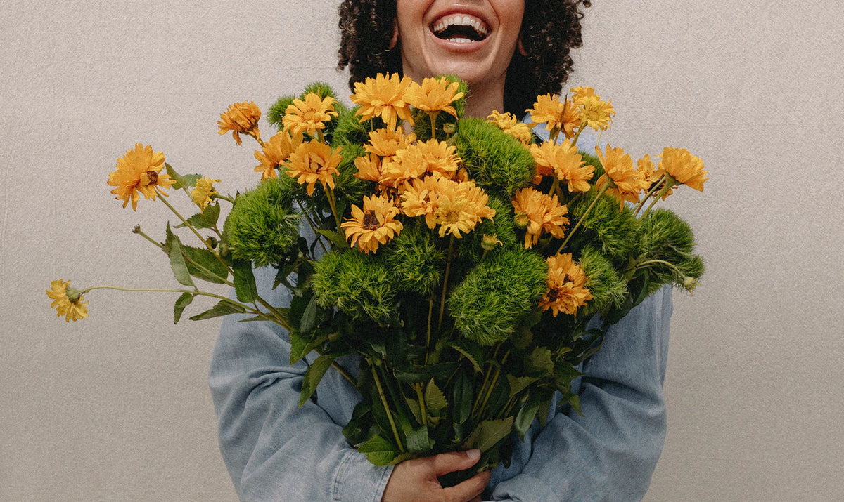 A woman laughing behind an armful of yellow flowers