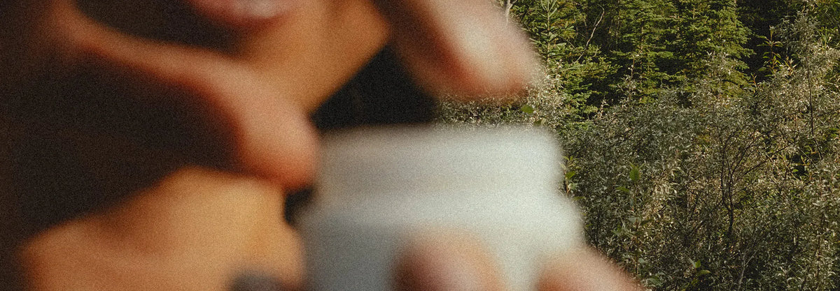 Hands opening a jar of Essential Face Cream in the forest