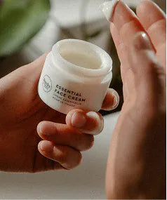 A hand holding an open jar of Essential Face Cream